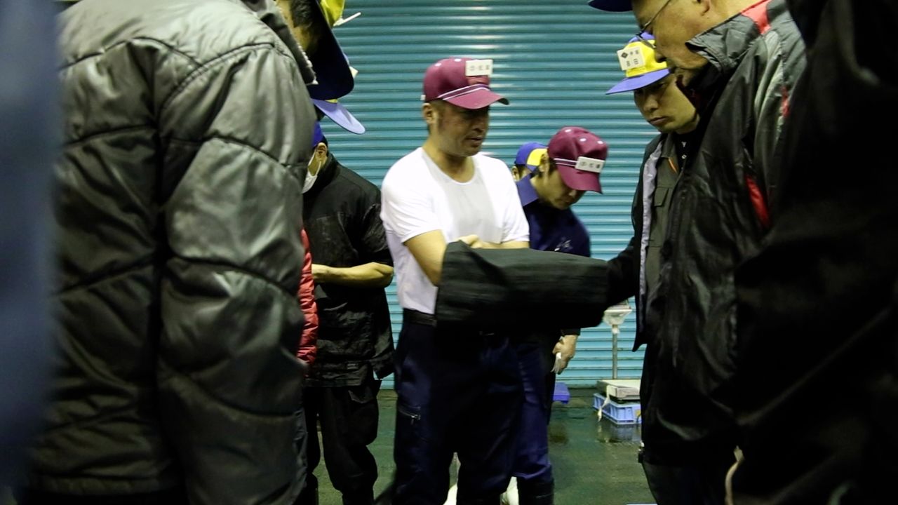 南風泊市場內的傳統河豚「袋競價」。仲介批發商在袋子裡以手指比劃數字來議價。© GUN FISH FILM PARTNERS
