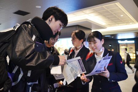 攜帶行動電源登機限2個的新規定將於24日展開,航空公司職員(右)於羽田機場向旅客進行宣導。14日下午