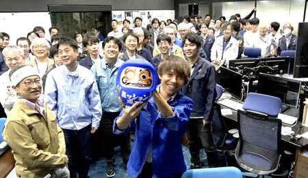 在探測器「隼鳥2號」成功完成小行星「鳥船」的飛掠觀測(Flyby)後,隼鳥2號擴展任務團隊負責人三桝裕也手拿達摩不倒翁在管制室內慶祝=5 日下午(摘自 JAXA 官方 YouTube)