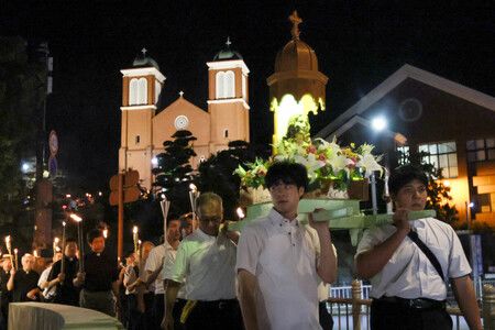 為悼念原爆罹難者,參加者抬著「被爆聖母像」(右上),從浦上天主堂(左後方)前往爆心地公園的火炬遊行。9日下午、長崎市
