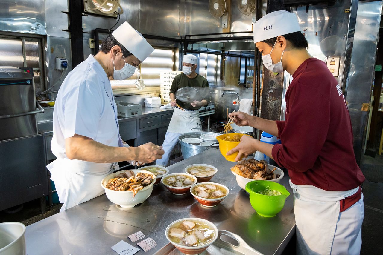 الطهاة مشغولون بتحضير الطعام داخل مطبخ مطعم باناي شوكودو الأكثر شهرة في مدينة كيتاكاتا، حيث يبدأ رواد المطعم في التدفق بدأً من السابعة صباحاً.
