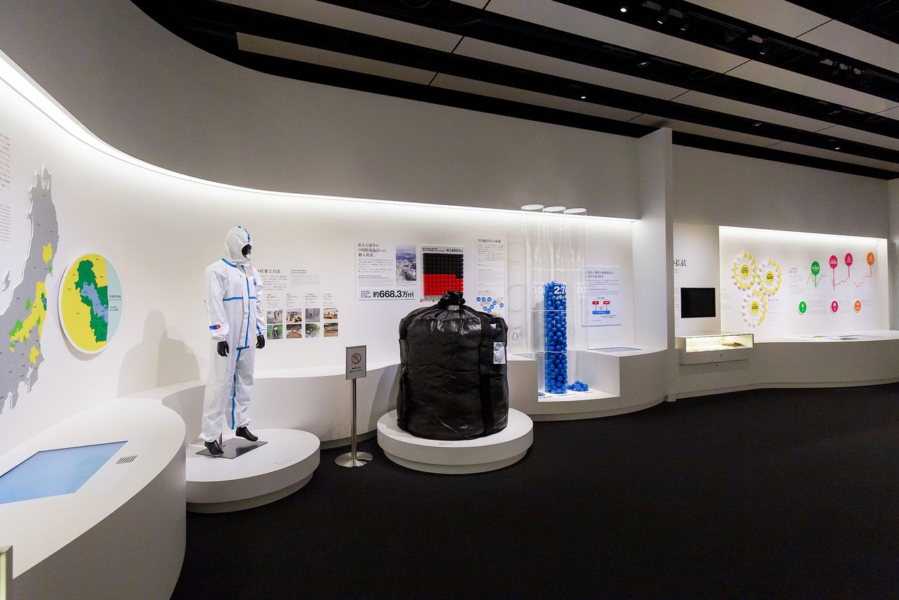 جانب من المعروضات يضم سترة واقية من المواد الخطرة مثل تلك التي يرتديها العمال المشاركون في جهود إزالة الملوثات جنبًا إلى جنب مع كيس يستخدم لحمل النفايات الملوثة.