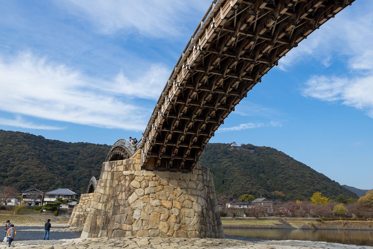 النظر إلى الجسر من ضفة النهر يكشف عن فنون النجارة والتركيبات الخشبية المعقدة المستخدمة في بنائه.