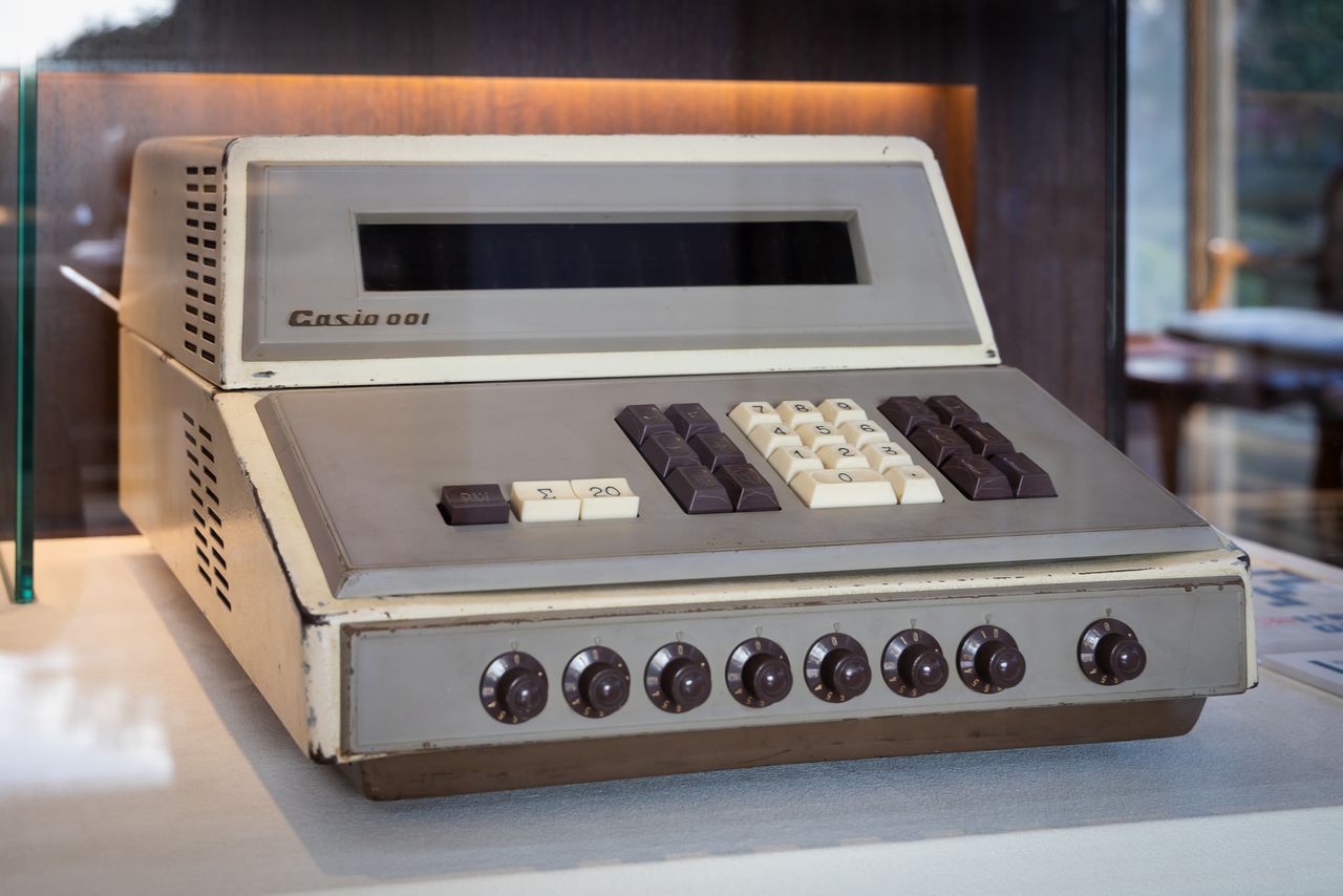  أول آلة حاسبة مكتبية إلكترونية ”001“ لشركة كاسيو. كان الحرف الأول فقط من شعار الشركة مكتوبا بأحرف كبيرة آنذاك.