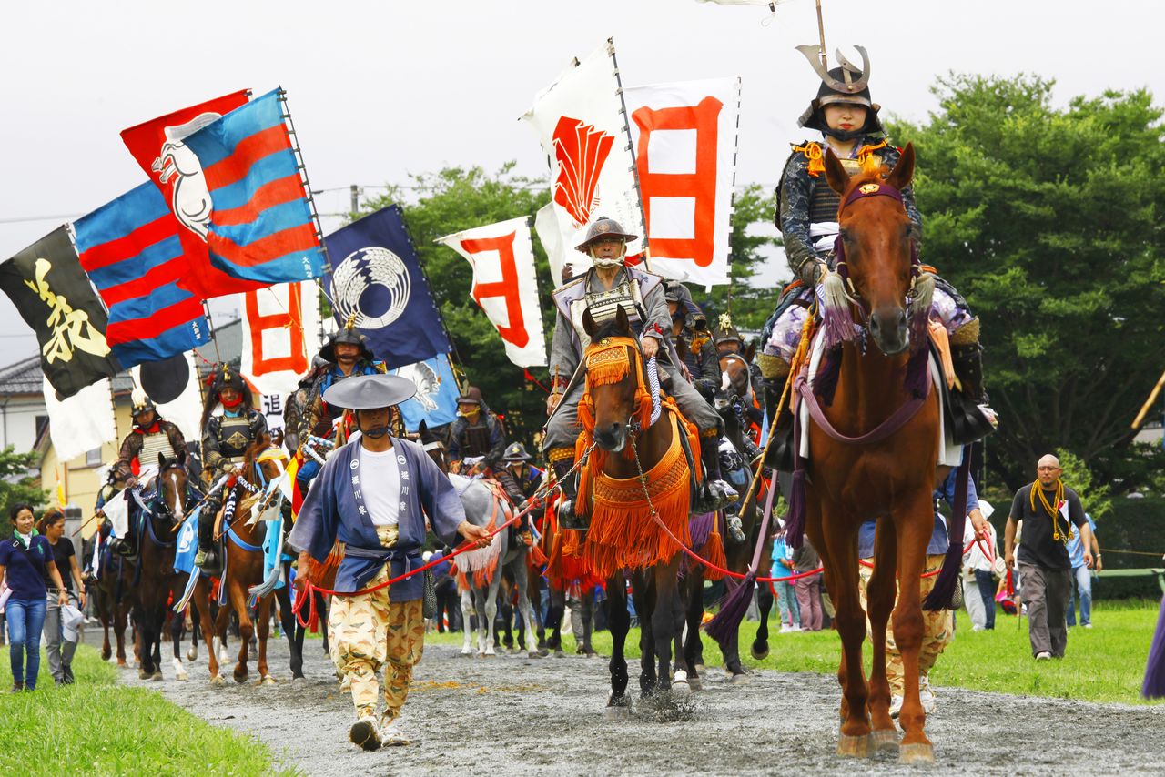 صورة لفرسان بزي مقاتلي الساموراي يحملون أعلاماً إحياءً لطقوس قديمة ”© مكتبة هاغا“