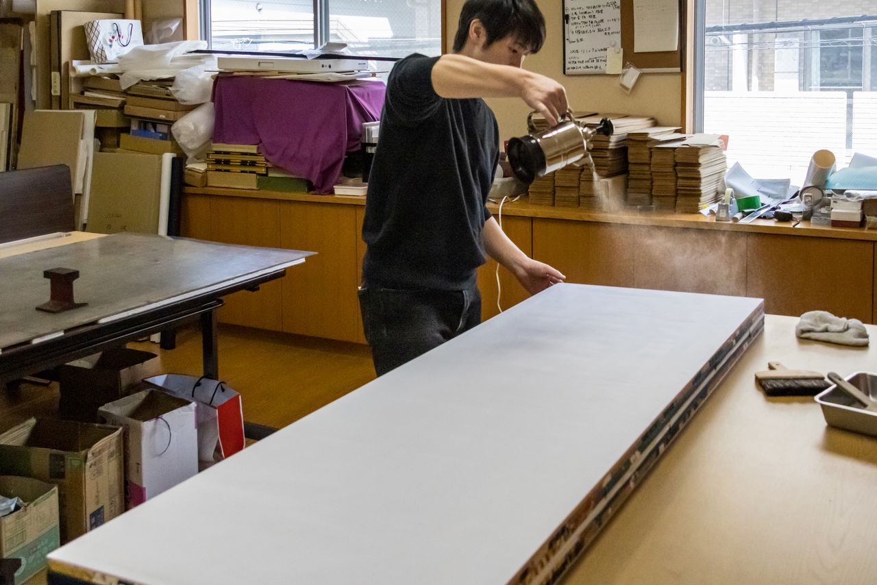 يستخدم أحد الحرفيين في ورشة ”كاتاؤكا بيوبو“ تقنية تقليدية لتنعيم سطح السواتر القابلة للطي استعدادًا للطباعة. (© Nippon.com)