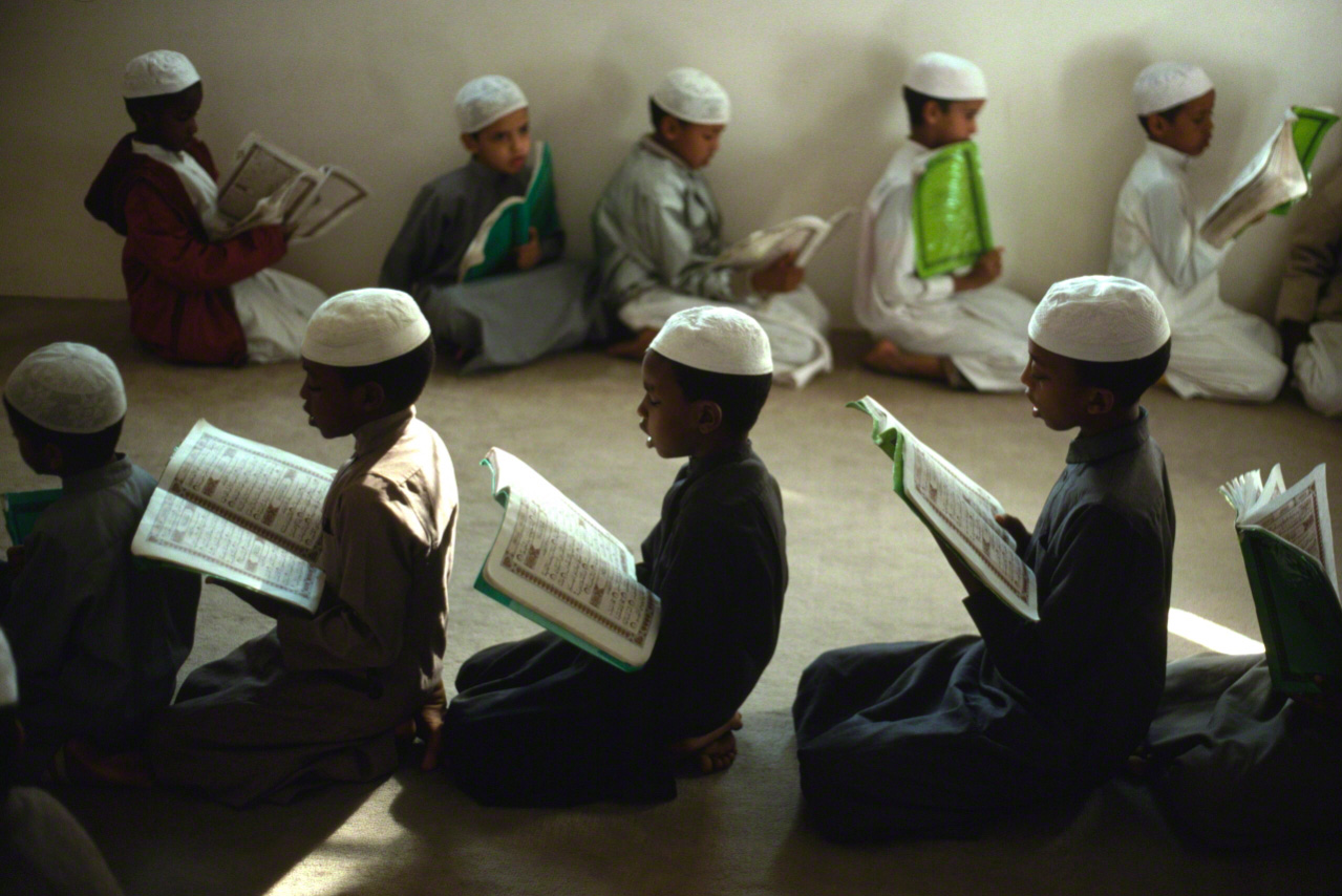 أطفال العمال الأجانب وهم يتعلمون القرآن في صف لتعليم القرآن في المدينة المنورة في السعودية. تم التقاط الصورة في عام 1997. من كتاب ”حج مكة“.