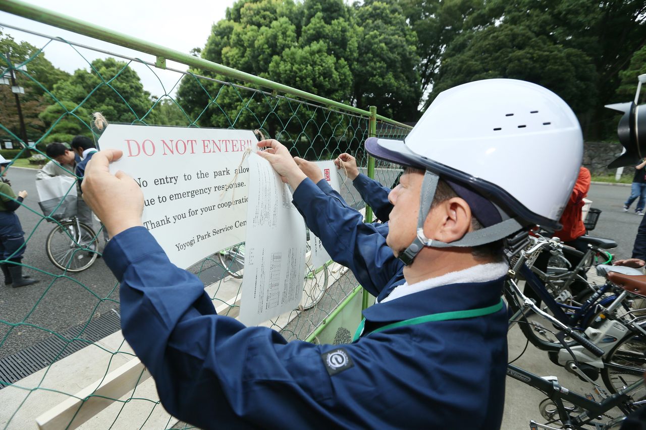 موظفو متنزه يويوغي في 4 سبتمبر/أيلول عام 2014 يضعون ملصقات تشير إلى الإغلاق المؤقت للمتنزه الذي يقع في طوكيو بعد اكتشاف البعوض الذي يحمل فيروس حمى الضنك (حقوق الصورة لجيجي برس).