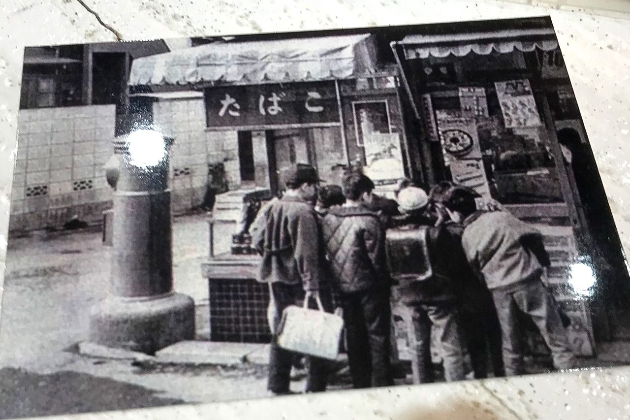 أطفال مجتمعون أمام متجر للحلوى. كانت معظم الآلات تتقاضى 10 ينات في ذلك الوقت (نُشر ت الصورة في الأصل في مجلة Asahi Graph عام 1966، من أرشيف أونو).