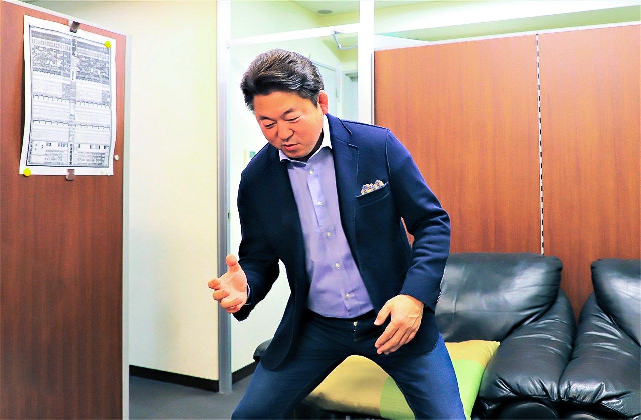  خلال المقابلة، كان ماينؤمي كثيرًا ما يقف ويومئ ليشرح حركاته. يتميز تعليقه خلال بث بطولات السومو على قناة إن إتش كيه بالوضوح والسلاسة وسهولة المتابعة. (Nippon.com)