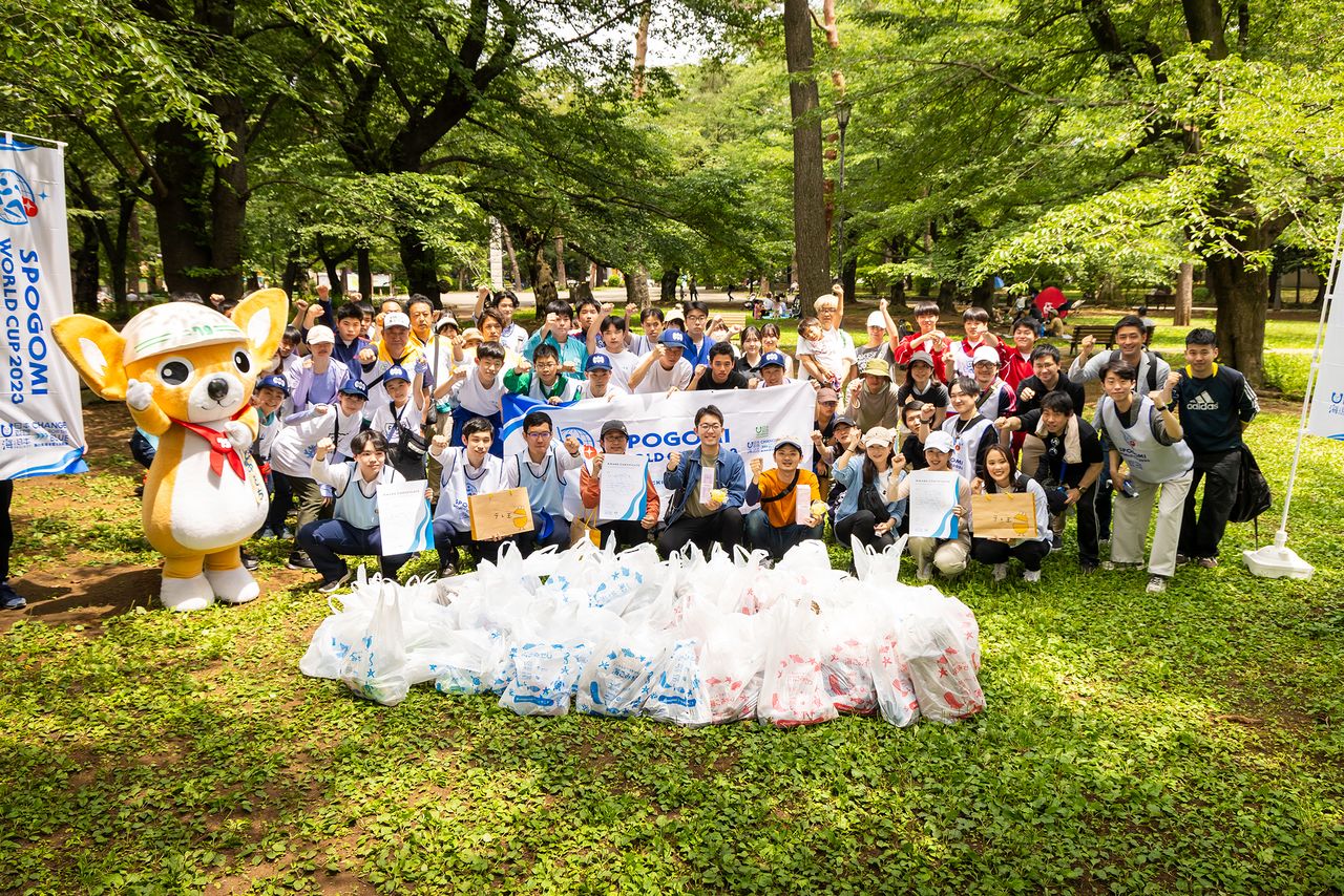  تقف فرق سايتاما المشاركة في المنافسة في نصف دائرة، حاملين أكياس القمامة التي جمعوها. يجلس الفريق الفائز المكون من ثلاثة أعضاء في منتصف الصف الأمامي (© nippon.com)