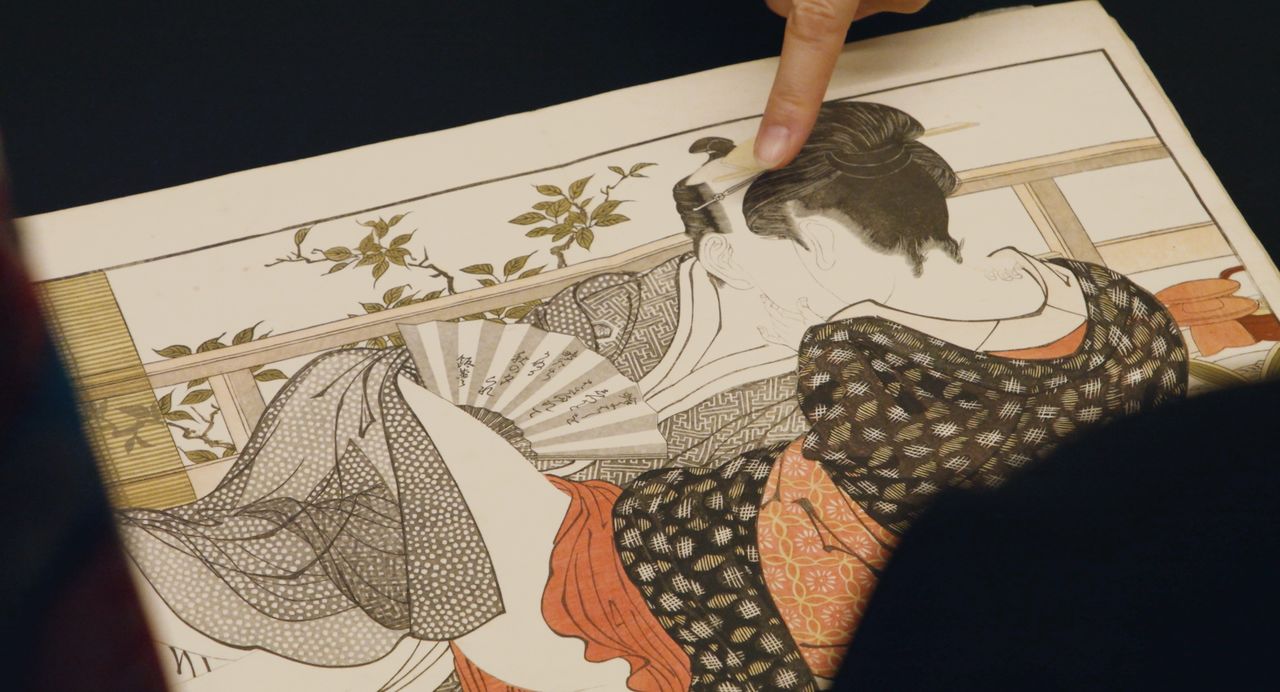 أوتا-ماكورا (قصيدة الوسادة)، وهي تحفة فنية رسمها كيتاغاوا أوتامارو (1753-1806)، من أبرز ما عرضه المعرض في المتحف البريطاني. في الجزء العلوي من الصورة، يشير خبير فني إلى عيني الرجل الضيقتين المرسومتين على خط بالقرب من شعر عشيقته (© 2023 لجنة إنتاج الشونغا)