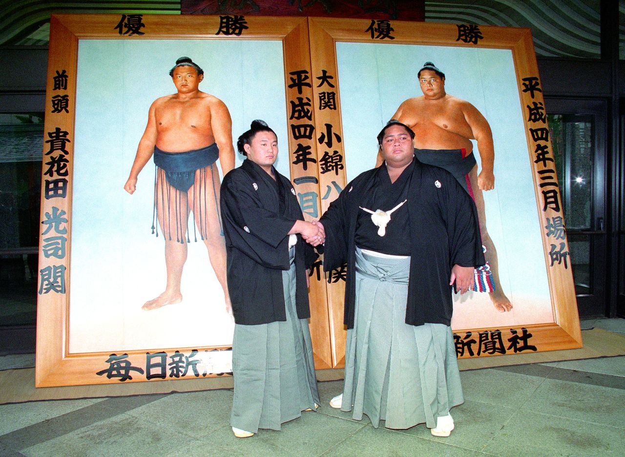 ميغاشيرا تاكاهانادا (على اليسار)، والذي سيُسمى فيما بعد باسم ˮتاكانوهانا“ سوف يستمر ليحصل على لقب يوكوزونا، وحامل لقب الـ ˮأوزيكي“ ˮكونيشيكي“ يقفان سويًا مع صور البطولة في حفل إزاحة الستار في طوكيو عام 1992. حيث كان عرض صور الفائزين في المسابقتين السابقتين يقام في اليوم السابق لبدء كل من البطولات الثلاث التي تقام في حلبة ˮكوكوغيكانˮ بطوكيو. (© جيجي برس)