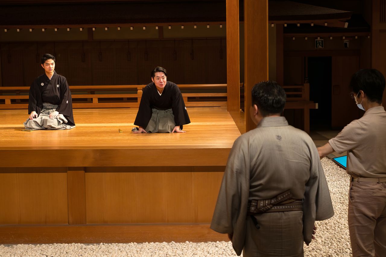 تاكانوسوكي ونومورا يوكي يتدربان على رقصة نينين سانباسو. يقف على اليمين نومورا مانساي الثاني والد يوكي ومصمم الرقصات الشهير فوجيما كانجورو الثامن، وهما يقدمان التعليمات (© ماتسودا تاداو، بإذن من مكتب تاكايا).