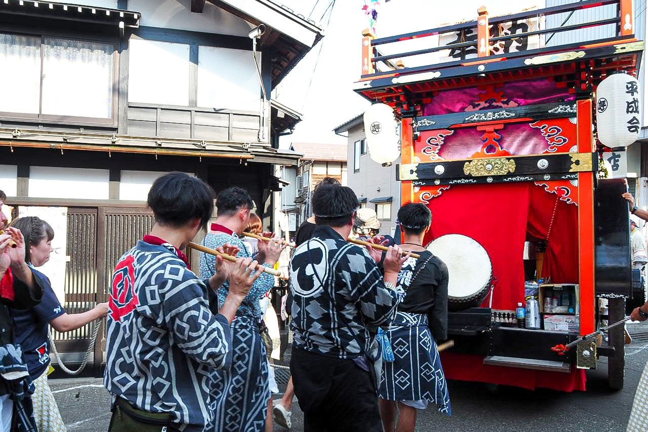 مشاركون في الموكب يعزفون الموسيقى أثناء سيرهم في أرجاء البلدة (© شينوهارا تاداشي). .