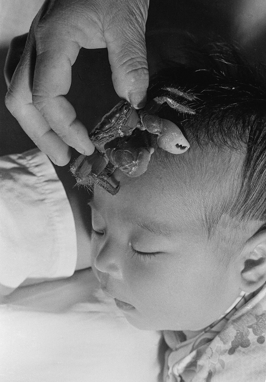 ”نانوكا إيواي“: يُوضع سلطعون على رأس طفل عمره سبعة أيام. حيث يُعبّر هذا الاحتفال عن تمني اجتياز الطفل المرحلة التالية من حياته المبكرة، زاحفًا كالسلطعون. جزيرة أوكينويرابوجيما، محافظة كاغوشيما، 1956. (© هاغا هيدييو)