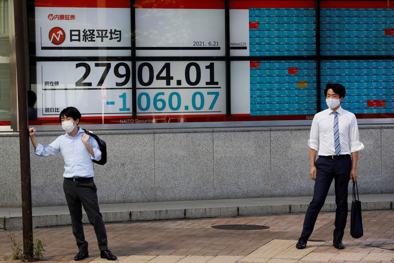 رجلان يقفان أمام شاشة إلكترونية تعرض مؤشر نيكي أمام مكتب للسمسرة في طوكيو يوم 21 يونيو حزيران 2021. تصوير: كيم كيونج-هوون - رويترز.