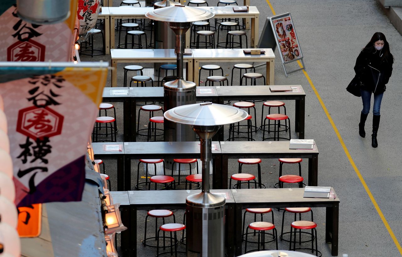 امرأة ترتدي قناعًا واقيًا من فيروس كورونا المستجد، تمر عبر طاولات فارغة في مطعم في شيبويا في طوكيو، اليابان، 7 يناير/ كانون الثاني 2021. رويترز / كيم كيونغ هون. 