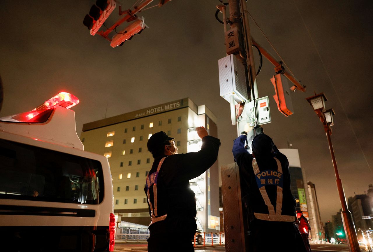 ضباط شرطة يحاولون إعادة تشغيل إشارات المرور عن طريق توصيل مولد كهربائي أثناء توقف كهربائي في المنطقة بعد زلزال طوكيو، اليابان، 17 مارس/ آذار 2022. رويترز.