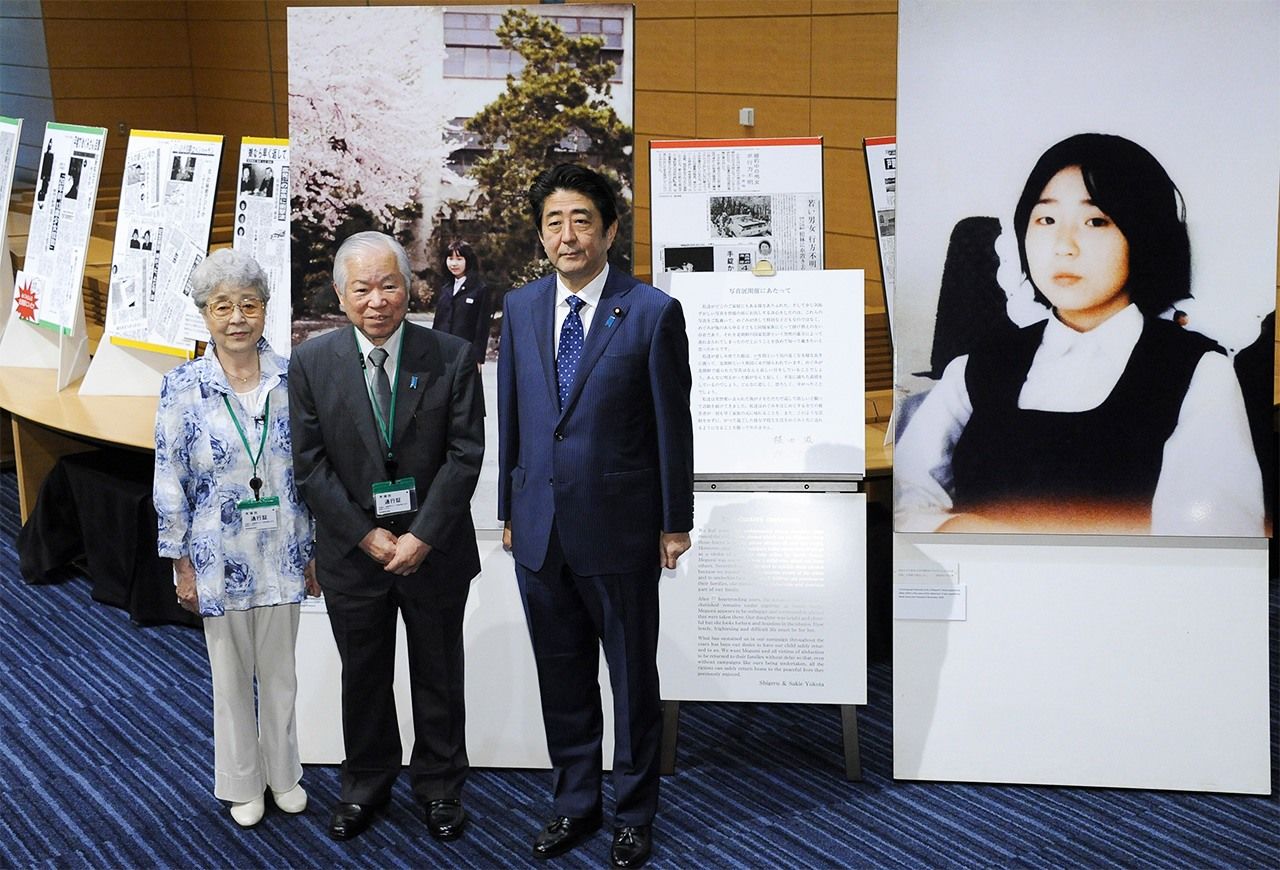 رئيس الوزراء شينزو آبى (يمين الصورة) مع (يوكوتا شيغيرو) (في الوسط) وزوجته (ساكي) في طوكيو في العاشر من يونيو/ حزيران. وعلى يمين الصورة تظهر لوحة لـ (يوكوتا ميغومي)، الفتاة التي كانت قد اختُطفت من قبل أحد عملاء كوريا الشمالية وهي في الثالثة عشرة من عمرها. جيجي برس.