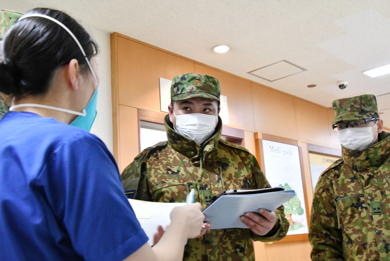 إحدى الممرضات من قوات الذاتي (على اليسار) تتحدث مع أعضاء آخرين في القوات في مستشفى كيوكاي يوشيدا في مدينة أساهيكاوا بمحافظة هوكايدو. (مكتب هيئة الأركان المشتركة، وزارة الدفاع، جيجي برس).