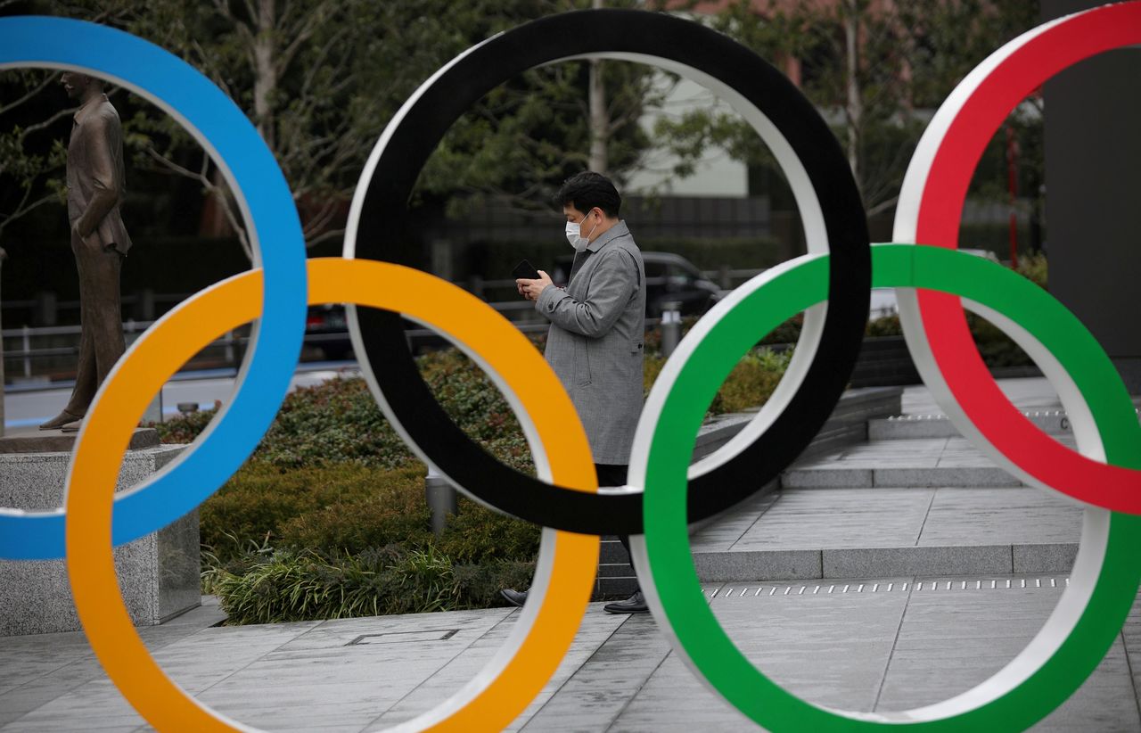 رجل ينظر إلى هاتفه المحمول بجوار الحلقات الأولمبية أمام متحف اليابان الأولمبي في طوكيو، اليابان، 4 مارس/ آذار 2020. رويترز / ستويان نينوف.