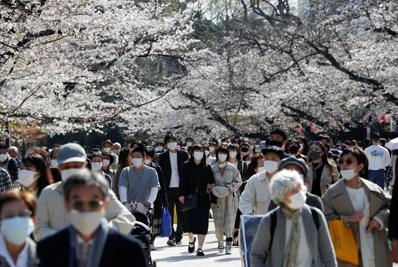 ينظر الزوار الذين يرتدون كمامات واقية بإعجاب إلى أزهار الكرز المتفتحة وسط جائحة فيروس كورونا (كوفيد-19)، في متنزه أوينو بطوكيو في اليابان، 23 مارس/آذار عام 2021. رويترز/إيسّيي كاتو.