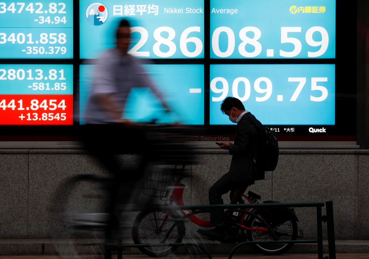 شخصان يركبان دراجتين هوائيتين يمران بشاشة تعرض مؤشر نيكي في طوكيو يوم 11 مايو أيار 2021. تصوير: إيسي كاتو - رويترز