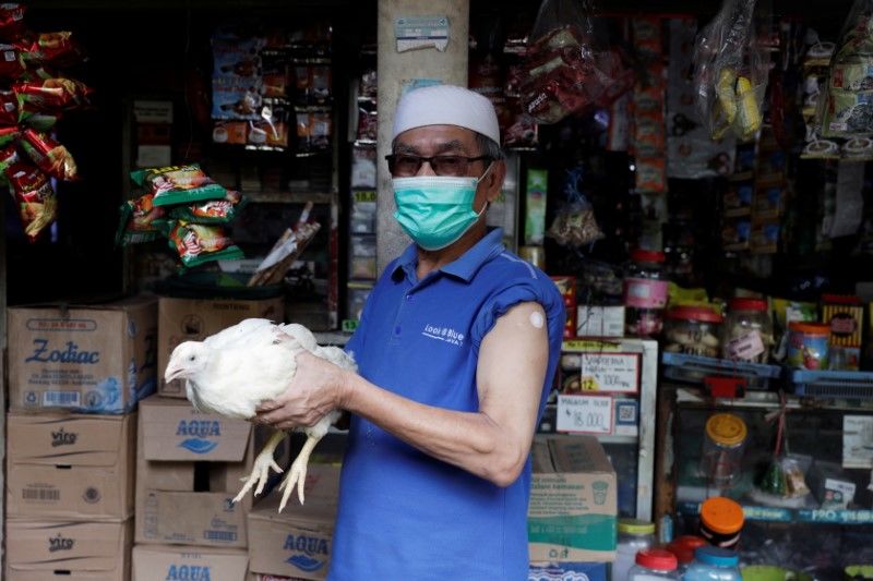 رجل يمسك دجاجة حية حصل عليها كجائزة بعد تلقيه الجرعة الأولى من اللقاح الواقي من فيروس كورونا في قرية بجاوة الغربية يوم الثلاثاء. تصوير: ويلي كورنياوان - رويترز