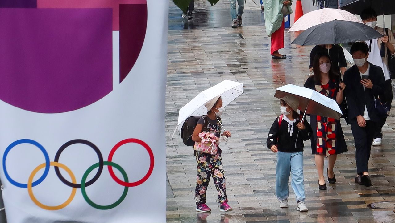  أشخاص يسيرون في أحد الشوارع بجوار إعلان عن دورة الألعاب الأولمبية طوكيو 2020، وسط جائحة فيروس كورونا، في طوكيو، اليابان، 19 يونيو/ حزيران 2021. رويترز / باول كوبتشينسكي.