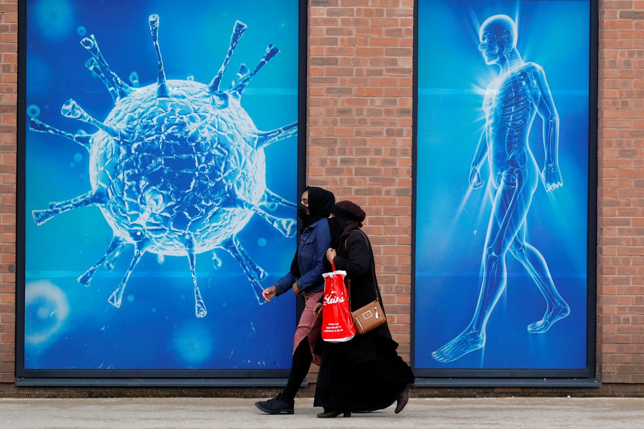 امرأتان تسيران أمام رسم توضيحي لفيروس كورونا في بريطانيا بصورة من أرشيف رويترز.