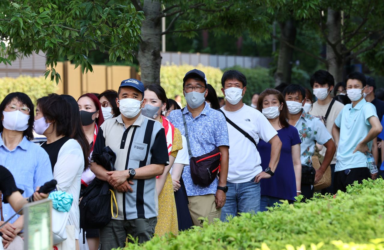 أشخاص يضعون كمامات للوقاية من فيروس كورونا يصطفون لالتقاط صور مع حلقة أولمبية في طوكيو يوم السبت. تصوير: كيم كيونج-هون - رويترز.
