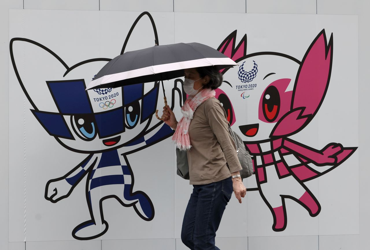 امرأة ترتدي قناعًا وقائيًا للوجه تمشي أمام زخرفة جدارية عليها تميمة أولمبياد طوكيو 2020 وتميمة الألعاب البارالمبية، وسط جائحة فيروس كورونا في طوكيو، اليابان في 28 مايو/ أيار 2021. رويترز / سترينجر.