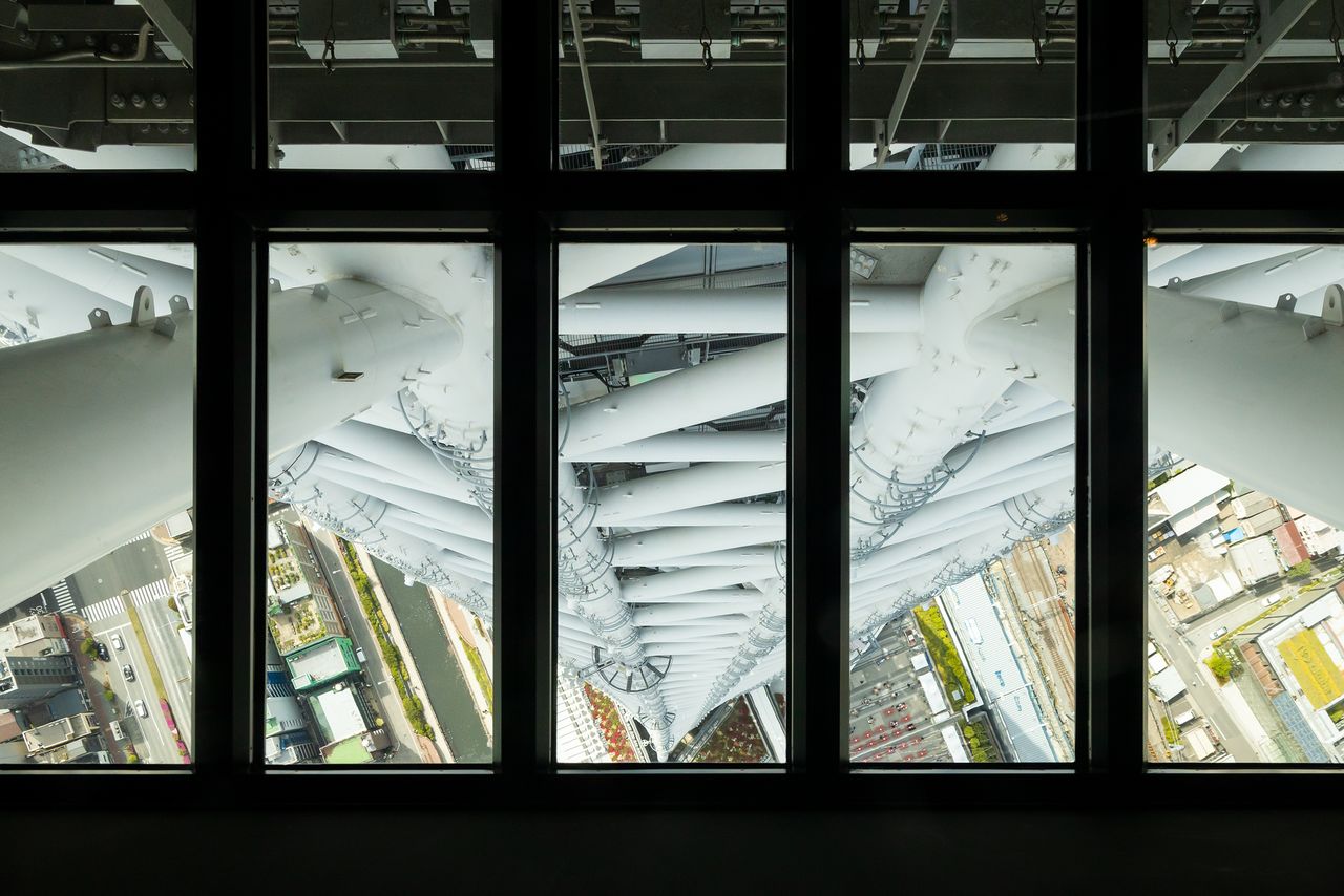 从天望甲板340楼的玻璃地板向下拍摄的照片。照片正中央的钢管在从三角形底座顶点向上延伸的过程中渐渐向内弯曲，其左右钢管微微向外隆起
