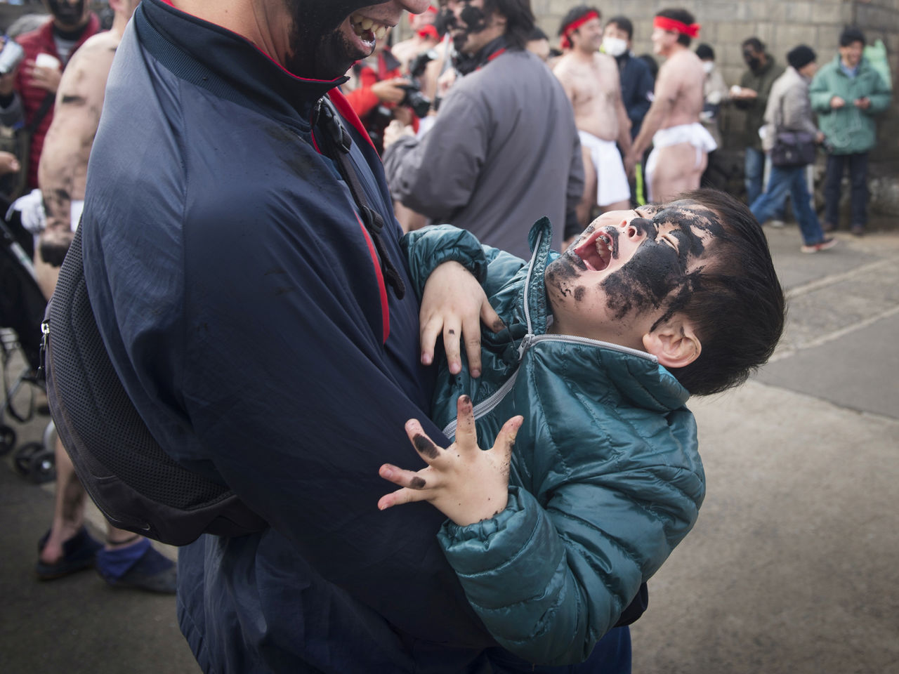 一个男孩儿脸上被涂满烟灰,放声大哭,孩子的父亲则欣慰地看着他