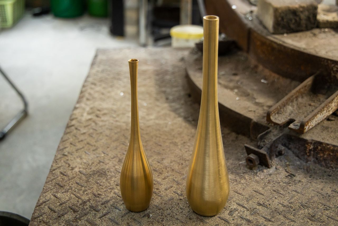 左边是神初先生最拿手的作品窄口流线型花瓶“鹤首”。与高冈铸器热门商品“Sorori”（右）花瓶相比，技术之精湛立判高下