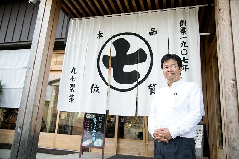铃木社长站在Nanaya店写有“创业于1907年”文字的门帘前