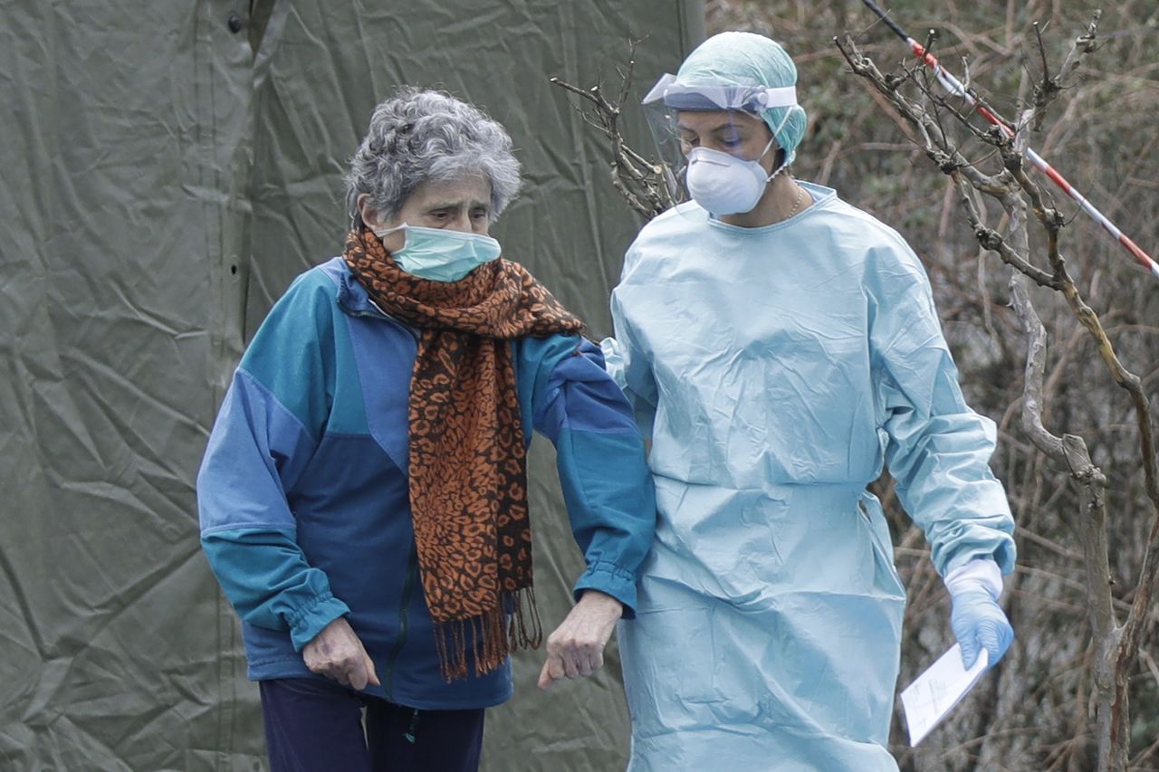 意大利北部伦巴第大区的布雷西亚市，穿着防护服的医生正在搀扶一位老年女性患者。截至3月12日，意大利的新冠病毒感染者达到15113人，死亡1016人。意大利成为继此次疫情最初爆发地中国之后，第二个死亡人数超过千人的国家（摄影：Luca Bruno／AP／Aflo）