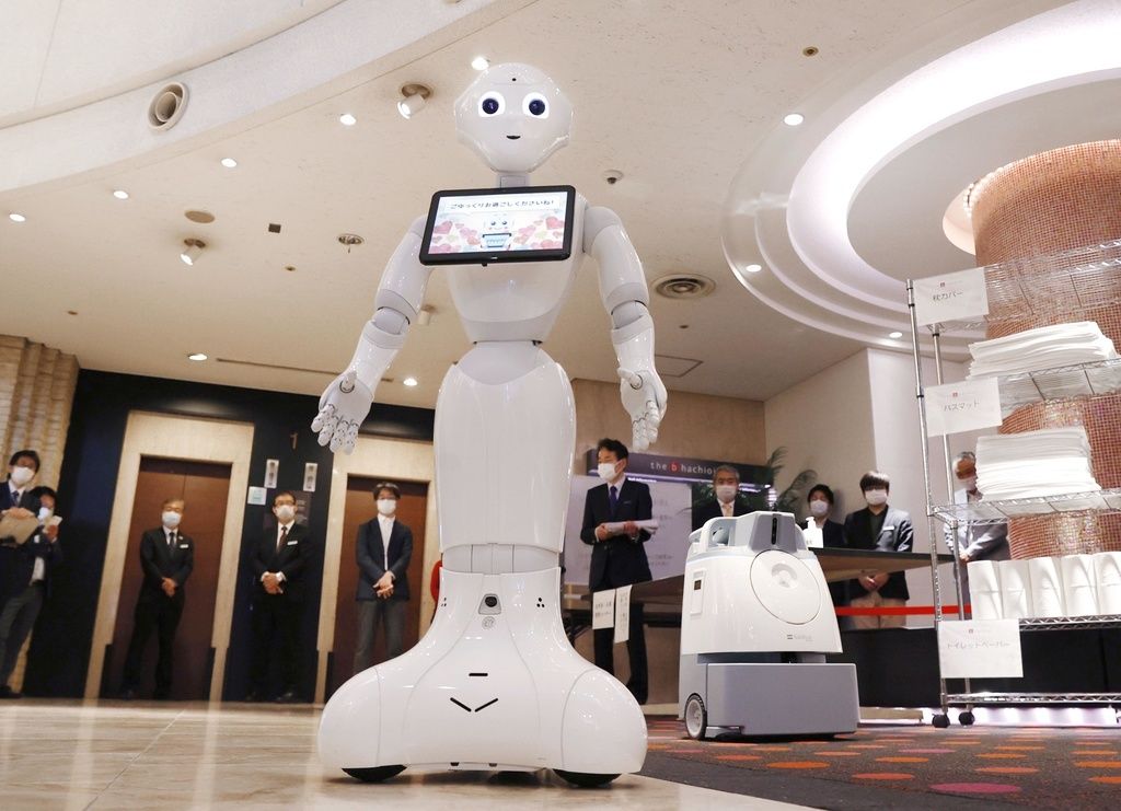 接收无症状或轻症新冠肺炎患者的酒店设施里，人形机器人“Pepper”出来迎客。右后方是具备人工智能的扫地机器人(2020年4月30日，东京都八王子市,共同社）