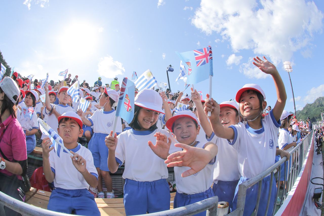 橄榄球世界杯斐济对乌拉圭的比赛中，当地小学生兴高采烈地挥舞两国国旗加油助威，2019年9月25日，岩手县釜石鹈住居复兴体育场（时事社）