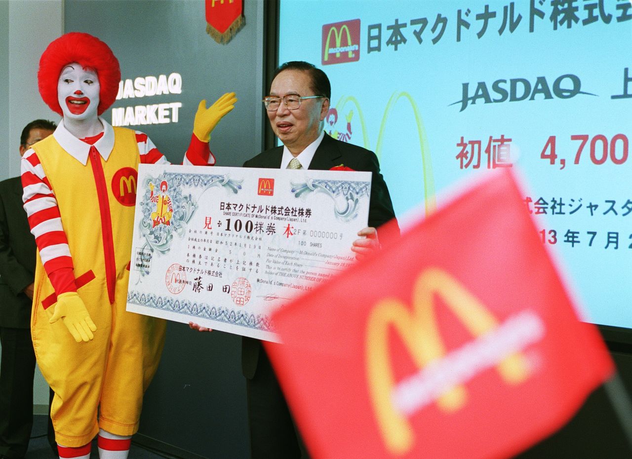 2001年7月26日，日本麦当劳公司在日本佳斯达克市场（JASDAQ）上市。在东京都中央区证券会馆举行的上市仪式上，藤田田社长和公司的吉祥物唐纳德一起向公众展示股票（图片：时事社）