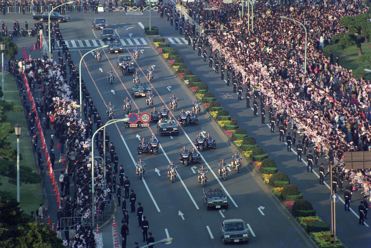 在平成时代的“祝贺御列之仪”中，天皇和皇后（现在的上皇夫妇）的车队在沿途民众的注目下前进，1990年11月12日，东京千代田区内堀大道祝田桥十字路口（读卖新闻社／Aflo）