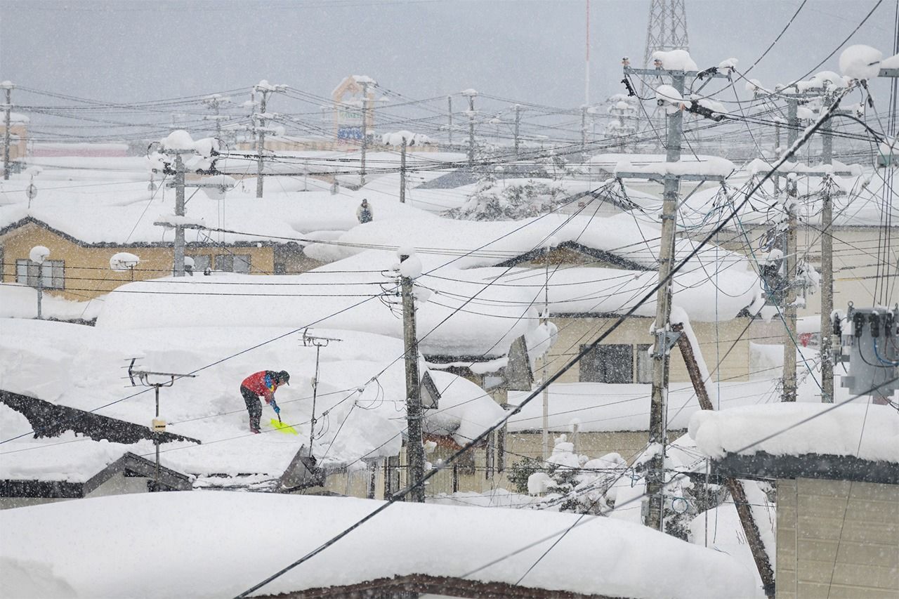 秋田县汤泽市。在屋顶铲除积雪的居民（Pixta）