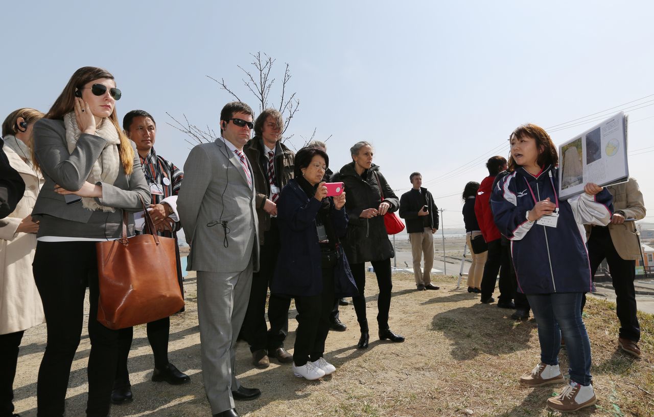 世界防灾大会的与会者们造访因海啸而受创的閖上地区，由“閖上震灾记念会”的女性成员（右侧）说明地震时的亲身经历（2015年3月17日，宫城县名取市，时事社）