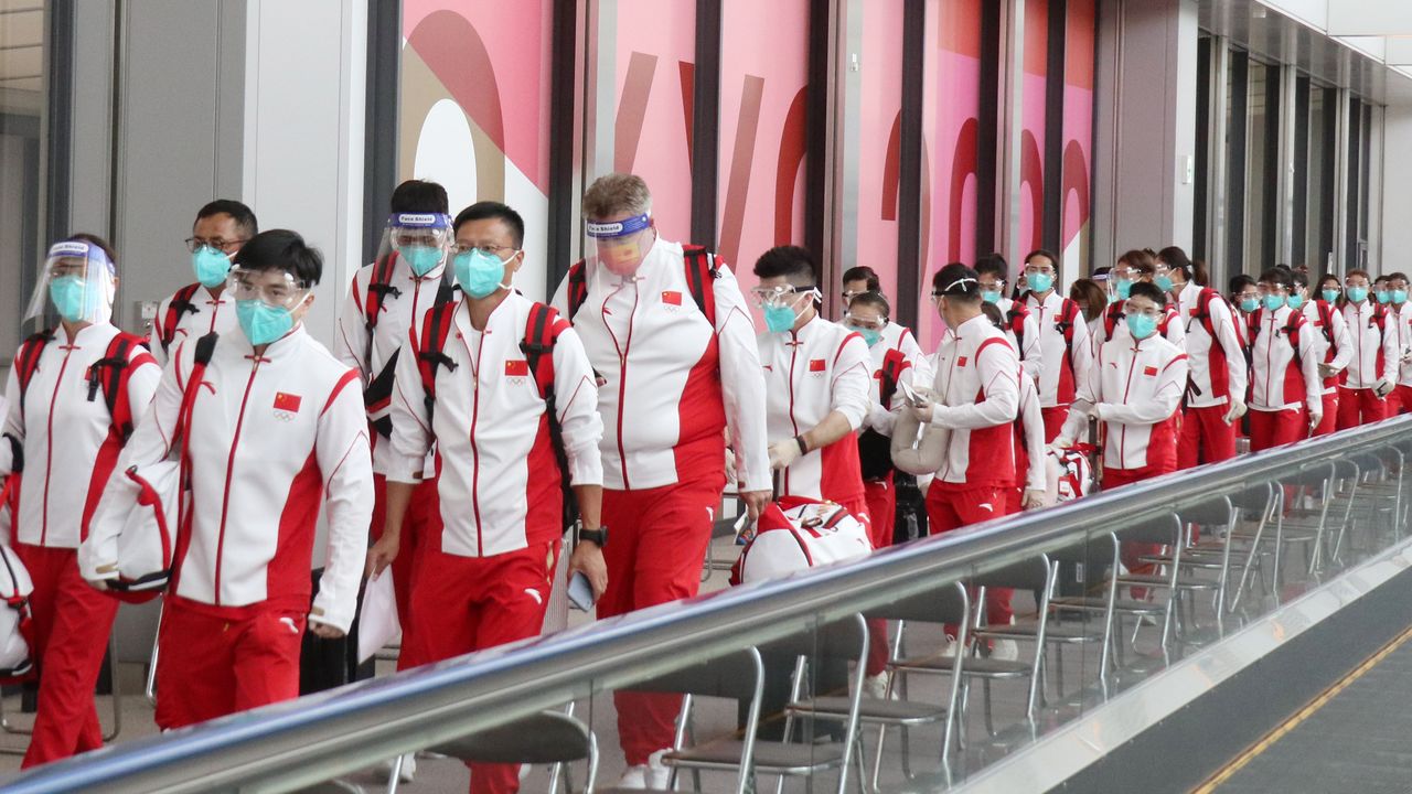 佩戴着面罩和口罩，整齐列队前往检疫站的中国代表团的运动员们（18日于成田机场，时事社）