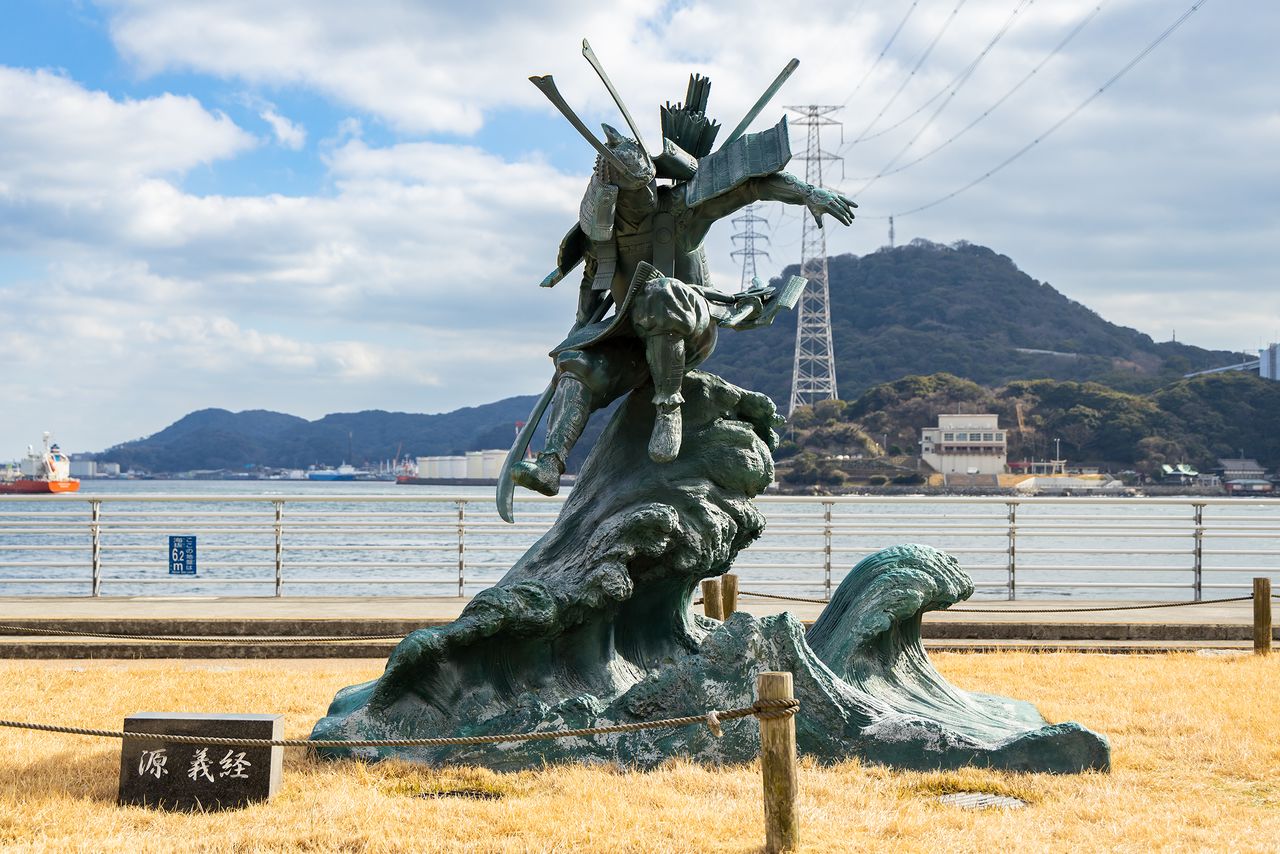 Statue of Yoshitsune, in heavy armor, leaping over eight boats.