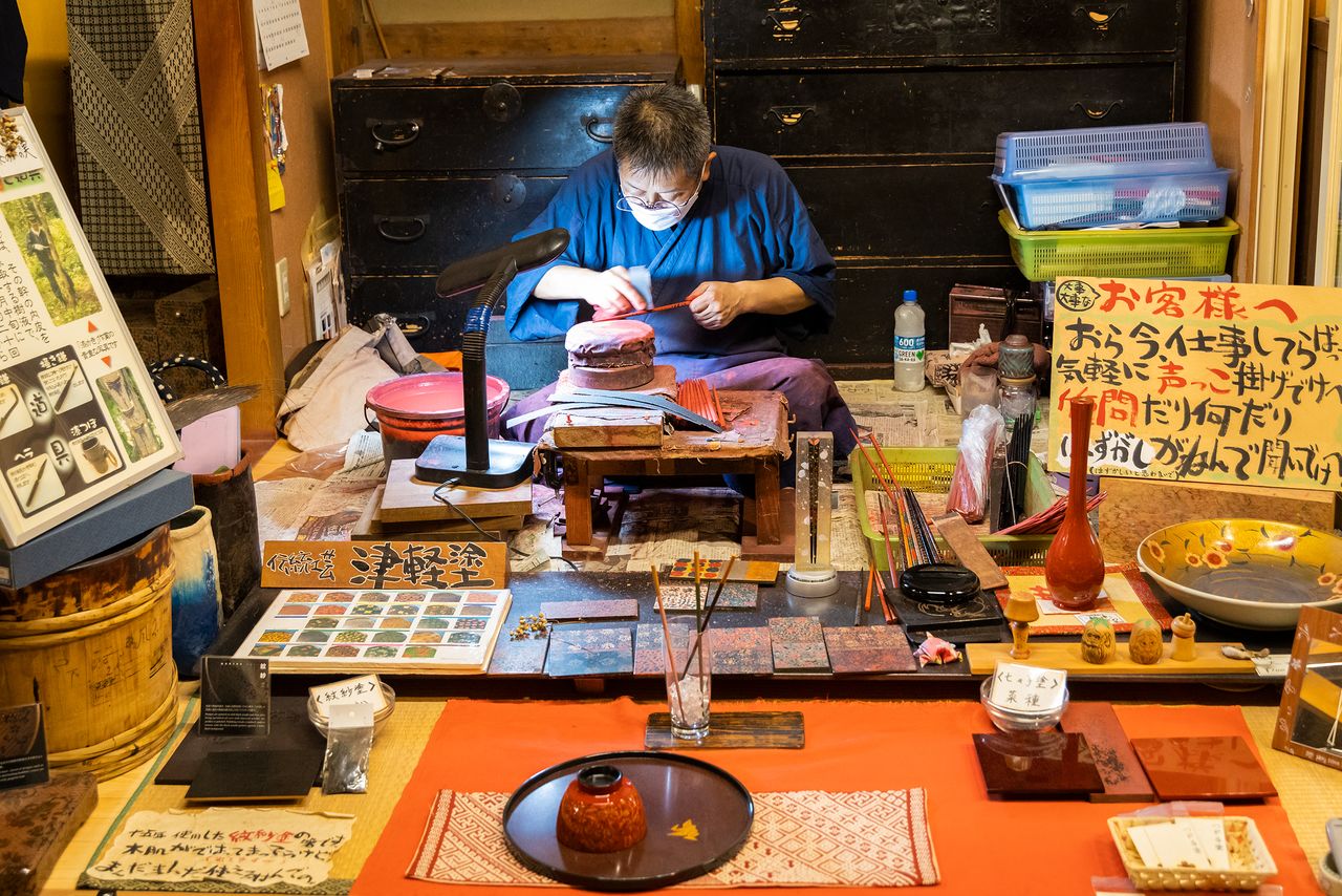 An artisan works on a piece of Tsugaru lacquerware. Visitors are welcome to ask questions.