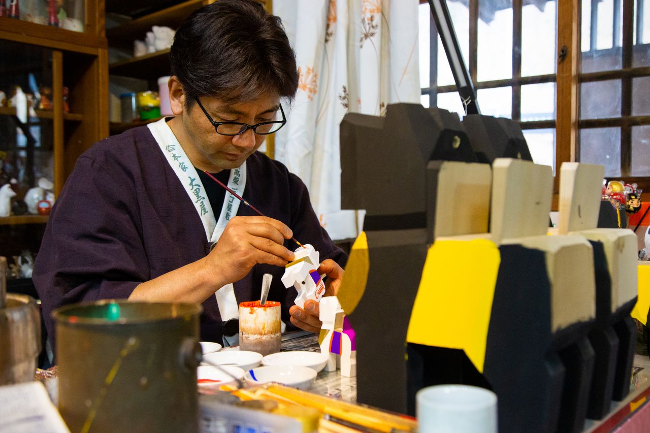 Hashimoto in a corner of his shop, painting a design onto a Miharu-goma figure.