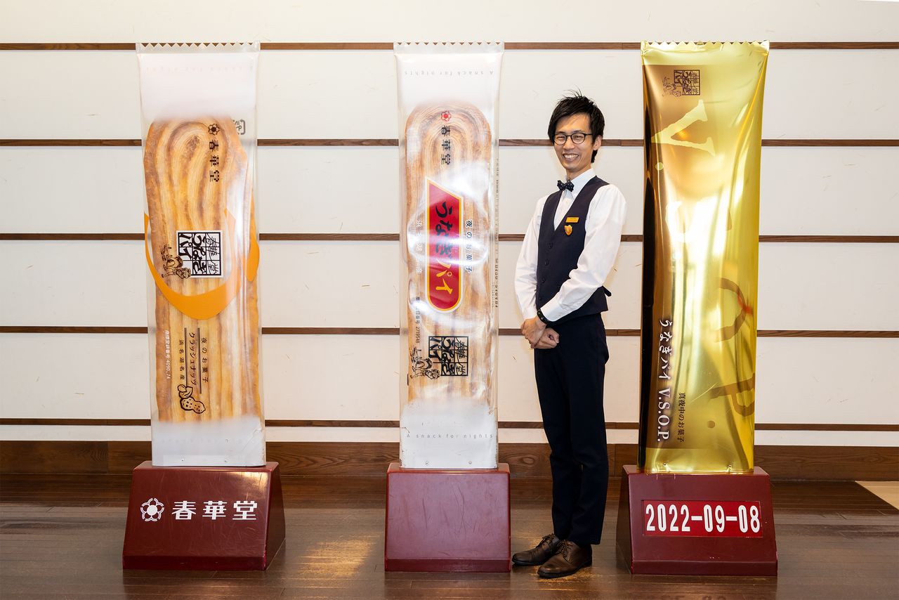 Guide Takyō Yūya poses next to giant reproductions of Unagipie and other popular Shunkadō products.