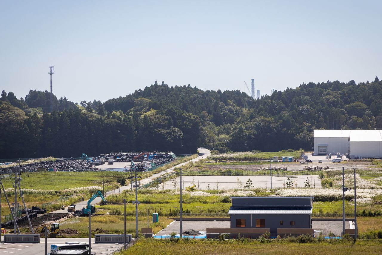 Interim radioactive waste storage facilities stand directly to the south. Fukushima Daiichi’s exhaust stacks are visible beyond the hills.